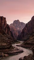 Dramatic canyon landscape with towering red rock cliffs framing a winding river flowing through the valley under a soft pink sunset sky, suitable for travel and nature backgrounds.