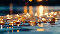 Glowing candles floating on water surface create magical bokeh effect with warm golden lights reflecting and rippling in dark blue water at dusk.