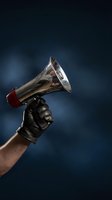 Hand in black leather glove holding chrome megaphone against dark blue background for protest communication and announcement campaigns.