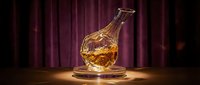 Elegant crystal whiskey decanter with amber liquid on wooden surface against luxurious burgundy curtain backdrop for premium bar and dining concepts.