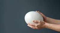 Caucasian male hands holding white spherical object against neutral gray background, suitable for business, technology, and conceptual design projects.