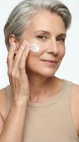 Mature woman applying face cream for anti-aging skincare routine on white background.