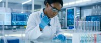 Male scientist of South Asian descent wearing protective eyewear and blue gloves conducting laboratory research with test tubes and samples in modern facility.