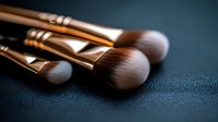 Professional makeup brushes with soft bristles and metallic gold handles on dark textured background, close-up view for cosmetics and beauty industry use.