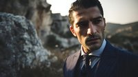Middle Eastern businessman in navy pinstripe suit with serious expression against rocky landscape at sunset, conveying confidence and determination.