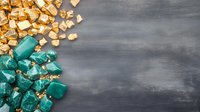 Scattered gold and turquoise crystal mineral chunks on dark textured background with copy space, forming decorative corner arrangement for luxury design.