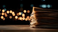 Stack of old paper documents with worn edges against dark background with golden bokeh lights creating nostalgic atmosphere for business and archive concepts.