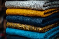 Stack of folded cozy winter sweaters in trendy colors - grey, mustard yellow, navy blue and turquoise. Warm knitted wool clothing texture close up.