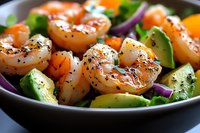 Fresh grilled shrimp salad with avocado slices, red onion, and herbs in dark bowl, seasoned with black pepper and spices for healthy lunch.