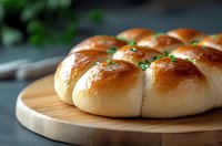 Freshly baked pull-apart dinner rolls with golden brown tops and garlic herb butter glaze served on wooden cutting board, soft and fluffy texture visible.