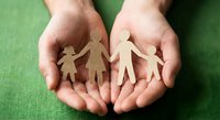Protective hands holding paper cutout family figures on green background symbolizing care, support, unity and family protection concept.