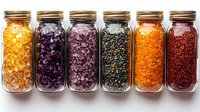 Colorful mineral bath salts in glass mason jars arranged in row on white background. Natural spa aromatherapy and wellness products for relaxation and skincare.