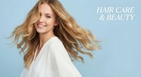 Young blonde woman with flowing hair in white shirt smiling against blue background for hair care and beauty advertising campaigns.