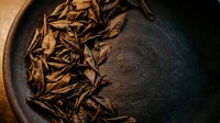 Dried cumin seeds in a dark ceramic bowl on black surface, overhead view for culinary and food styling projects.