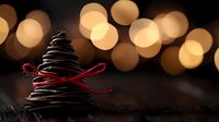 Chocolate cookie tree with red ribbon bow against blurred golden bokeh lights background creates festive holiday atmosphere and warmth.