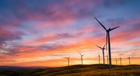 Wind turbines generating renewable energy against dramatic sunset sky with pink and orange clouds over rural landscape for sustainable power concepts.