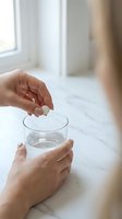 Woman taking white pill with glass of water on marble counter for daily medication routine and healthcare wellness.