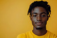 Young African American man with dreadlocks and yellow t-shirt smiling confidently against vibrant yellow background, modern portrait highlighting natural expression.