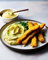 Crispy breaded fish sticks served with creamy herb-infused mashed potatoes and fresh chopped parsley on ceramic plate, comfort food meal.