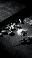 Drug addiction concept with pills, powder and syringe scattered on dark wooden surface in dramatic black and white lighting for awareness campaigns.