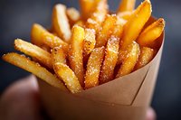 Crispy golden french fries sprinkled with salt in brown paper holder against dark background, close-up macro shot showing texture and seasoning details.