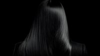 Long straight dark hair on black background, dramatic lighting highlights silky smooth texture and shine. Professional hair care and beauty concept.