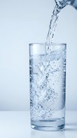 Fresh clear water pouring into transparent glass with bubbles and splash creating dynamic motion against clean white background for health and hydration concepts.
