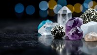 Collection of healing crystals and gemstones including amethyst, clear quartz, and pyrite arranged on dark surface with colorful bokeh lights background.