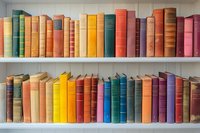 Colorful vintage hardcover books arranged on white wooden shelves in rainbow order, creating vibrant library display. Classic literature collection shows spines in various sizes.