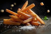 Crispy golden french fries sprinkled with salt crystals on dark background, dynamic food composition with flying salt particles in dramatic lighting.