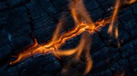 Molten lava flowing through cracks in dark volcanic rock surface creating dramatic orange glowing streams against charcoal textured stone background.