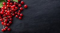 Fresh red currants with green leaves on dark slate background with copy space for culinary and healthy eating concepts.
