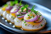 Pan-seared scallops garnished with purple onion rings, fresh herbs, and citrus segments served on dark plate with creamy sauce dots for fine dining.