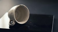 Ceramic mug tilted on dark surface with light casting shadow, suitable for beverage, kitchenware, and product mockup designs.