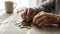 Senior adult hands arranging coins on table with cup nearby, depicting financial planning, savings, budgeting, retirement planning, money management and economic concerns.
