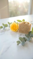 Handmade natural soap bar with exfoliating texture next to fresh yellow rose and eucalyptus leaves on marble surface, ideal for spa and wellness marketing.