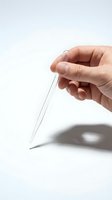 Hand holding clear glass pipette dropper with sharp tip against white background, suitable for medical, laboratory, pharmaceutical, and scientific research applications.