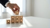 Businessman hand placing wooden cube with lightbulb icon on stack representing innovation, creativity and business solution development in office.
