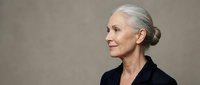 Elegant senior Caucasian businesswoman with gray hair in professional black blazer looking confidently to side against neutral background for corporate use.