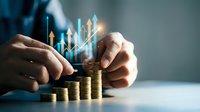 Businessman hands protecting golden coin stacks with rising arrow graphs showing financial growth and investment success in corporate environment.