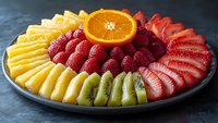 Fresh sliced tropical fruits arranged on gray plate including pineapple, orange, strawberries and kiwi. Colorful healthy fruit platter for party or catering.
