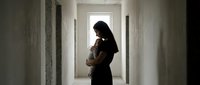 Young Asian woman tenderly holding newborn baby in empty unfinished corridor, soft natural light, motherhood and new beginnings concept.