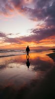 Silhouetted surfer holding board on wet beach at golden sunset with dramatic orange and purple sky, ocean waves, and reflection on sand for travel and lifestyle content.