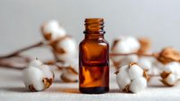 Amber essential oil bottle with cotton flowers on white textile background, natural skincare ingredient for aromatherapy and wellness treatments.