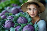 Young Caucasian woman in straw hat holding fresh purple cabbage at farmers market, representing healthy organic produce and farm-to-table lifestyle.