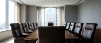 Modern corporate boardroom with dark leather chairs around polished conference table overlooking city skyline through large windows for business meetings.