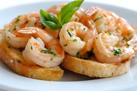 Succulent garlic shrimp served on toasted bread with fresh herbs and olive oil, close-up view on white plate, appetizing Mediterranean seafood starter.