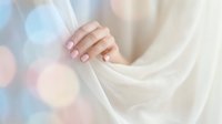 Young woman's hand with pink manicure holding soft white fabric, pastel bokeh background, elegant nail care and beauty concept.