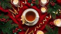 Festive Christmas tea cup surrounded by holiday decorations, candles, cinnamon sticks and evergreen branches on red background for seasonal celebrations.