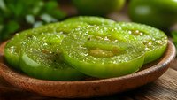 Fresh sliced green tomatoes on wooden plate with salt crystals visible, showcasing tangy unripe produce for southern cooking recipes.